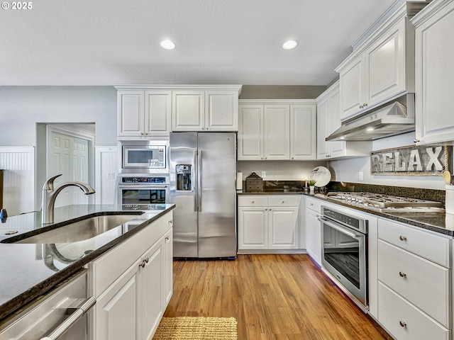 kitchen featuring stainless steel appliances, under cabinet range hood, a sink, white cabinetry, and recessed lighting