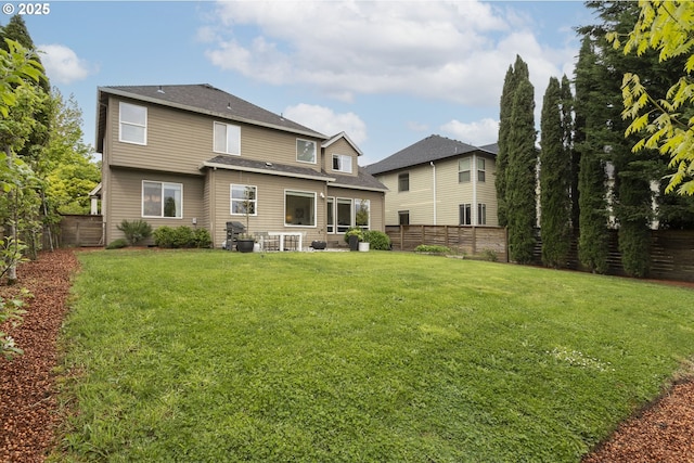 rear view of house featuring a yard, a shingled roof, and a fenced backyard