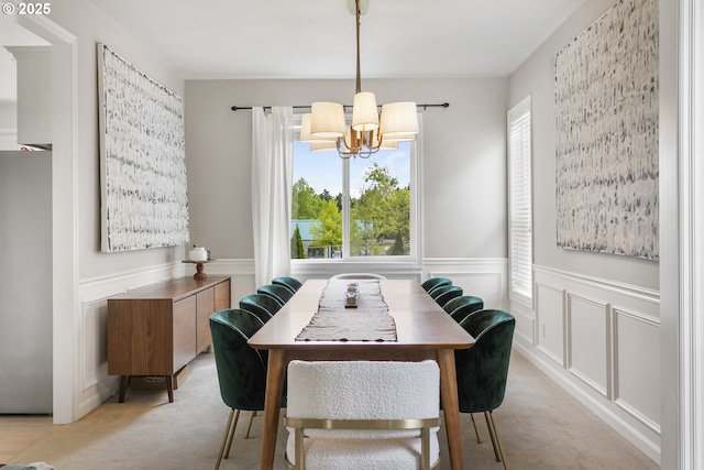 dining area featuring light colored carpet, a decorative wall, a wainscoted wall, and an inviting chandelier