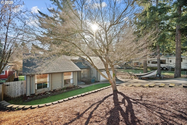 rear view of property featuring roof with shingles, fence, and dirt driveway