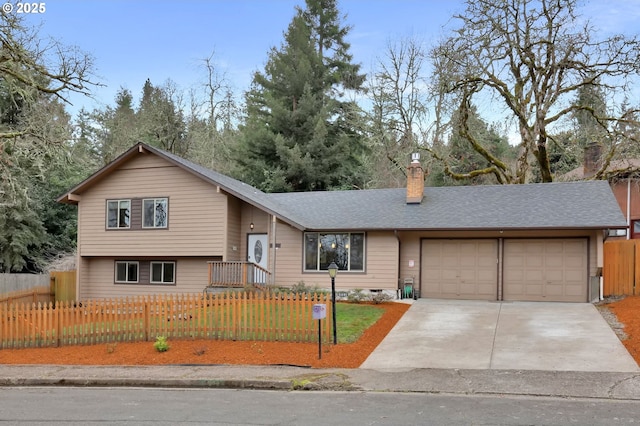 tri-level home with a fenced front yard, concrete driveway, a garage, and roof with shingles