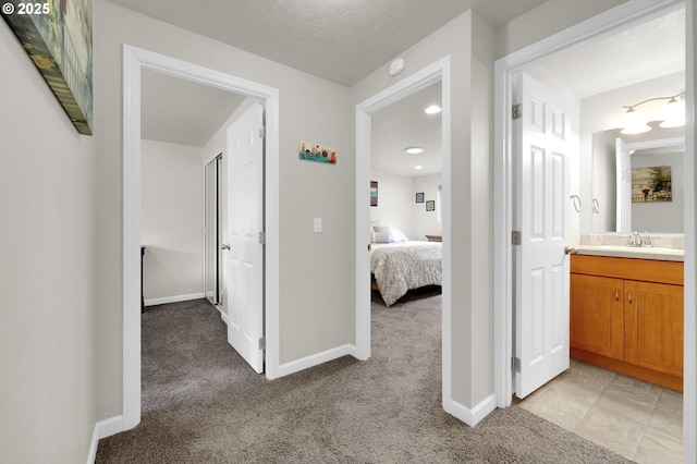 hallway with a sink, baseboards, light carpet, and a textured ceiling