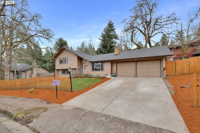 split level home featuring fence, roof with shingles, driveway, an attached garage, and a chimney