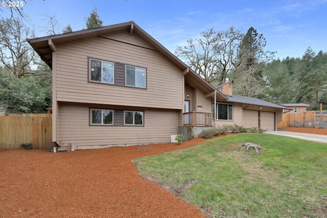 tri-level home featuring driveway, fence, a front yard, an attached garage, and a chimney