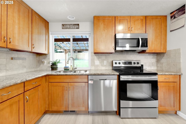 kitchen featuring a sink, stainless steel appliances, light stone counters, and backsplash