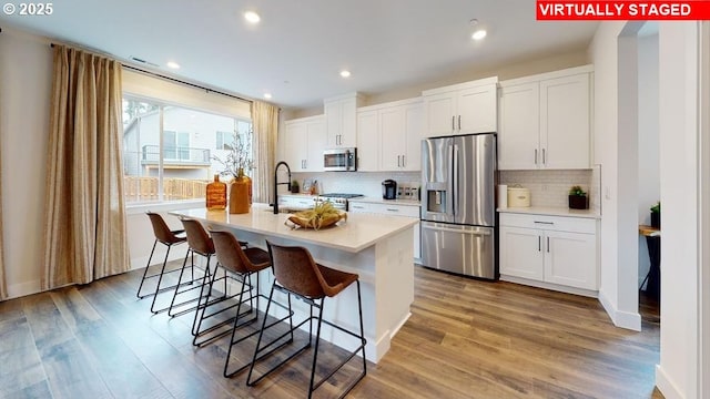 kitchen featuring wood-type flooring, stainless steel appliances, white cabinetry, and a kitchen island with sink