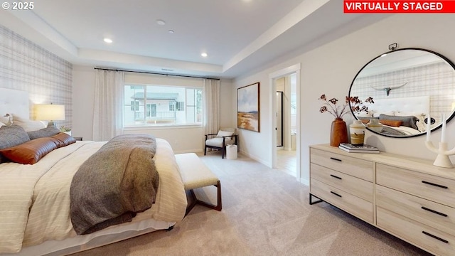 bedroom featuring a tray ceiling, ensuite bath, and light carpet