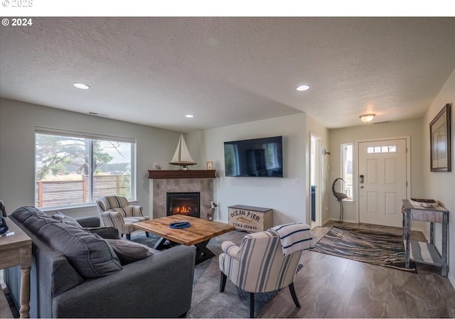 living area featuring recessed lighting, a textured ceiling, wood finished floors, and a tile fireplace