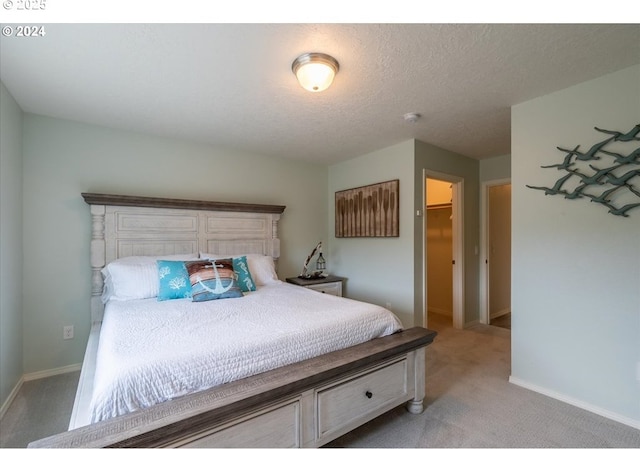 bedroom with a textured ceiling, baseboards, a walk in closet, and carpet flooring