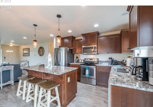 kitchen featuring appliances with stainless steel finishes, a center island, a sink, and light stone counters