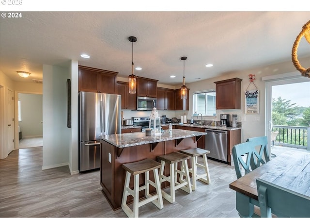 kitchen with a center island, a breakfast bar, stainless steel appliances, a sink, and light stone countertops