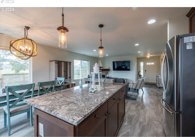 kitchen featuring light stone counters, visible vents, open floor plan, freestanding refrigerator, and decorative light fixtures