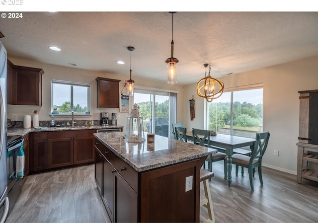 kitchen featuring a sink, plenty of natural light, a kitchen island, and light stone countertops