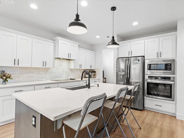 kitchen with white cabinetry, decorative light fixtures, a center island with sink, and appliances with stainless steel finishes