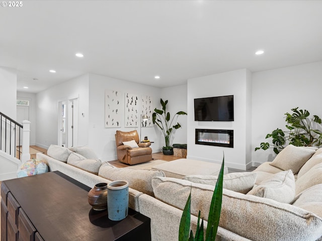 living room featuring a glass covered fireplace, baseboards, recessed lighting, and stairs