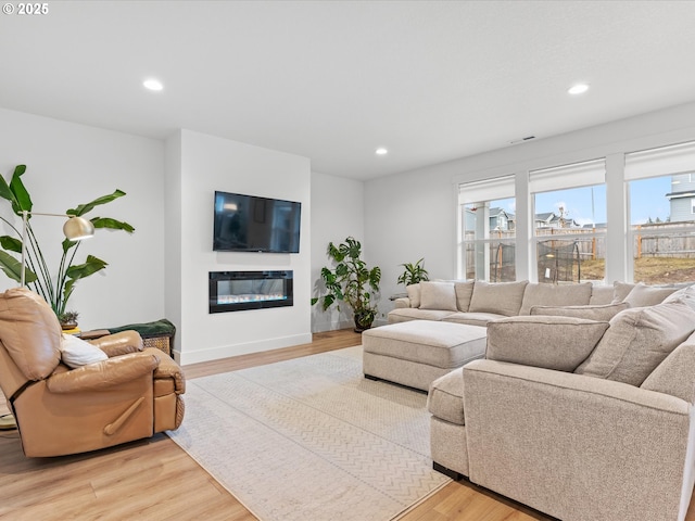 living area with baseboards, light wood-type flooring, a glass covered fireplace, and recessed lighting