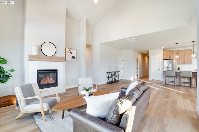 living room featuring high vaulted ceiling, a tiled fireplace, and light hardwood / wood-style floors