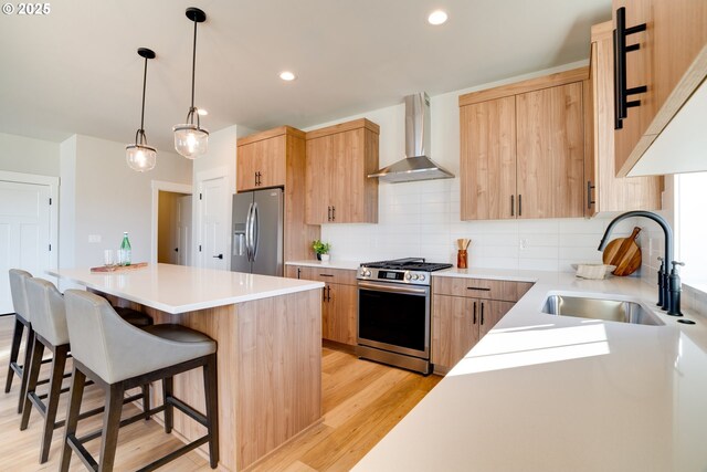 kitchen featuring sink, a center island, wall chimney exhaust hood, hanging light fixtures, and appliances with stainless steel finishes