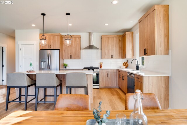 kitchen featuring stainless steel appliances, light wood-type flooring, a kitchen island, wall chimney range hood, and pendant lighting