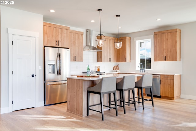 kitchen with hanging light fixtures, stainless steel appliances, a center island, light hardwood / wood-style floors, and wall chimney exhaust hood