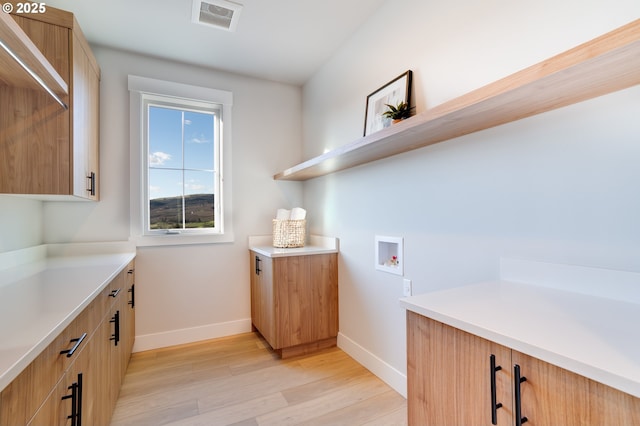 clothes washing area with cabinets, washer hookup, and light wood-type flooring