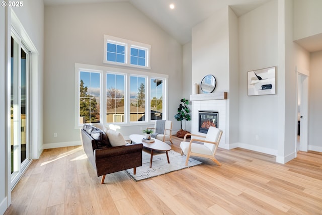 living room featuring a towering ceiling, a tiled fireplace, and light hardwood / wood-style floors