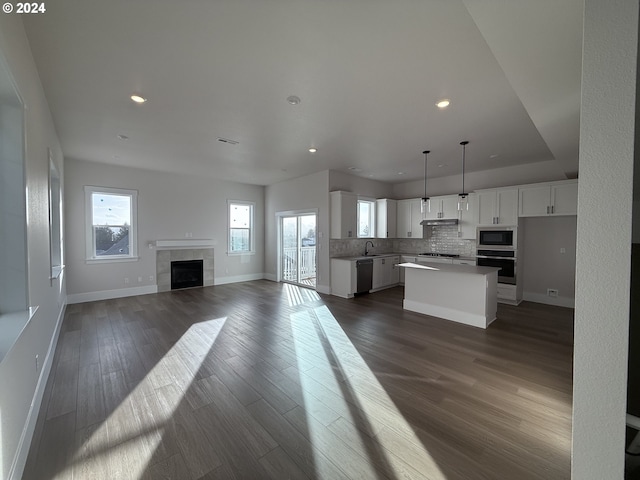 kitchen featuring white cabinets, a kitchen island, built in microwave, decorative light fixtures, and stainless steel oven