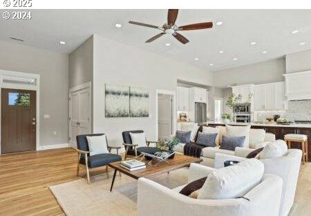 living room with a high ceiling, ceiling fan, and light hardwood / wood-style flooring