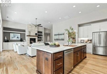 kitchen with sink, stainless steel appliances, a large fireplace, white cabinets, and a center island with sink