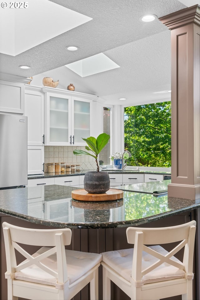 1433 SE 49th Ct, Hillsboro, OR 97123 - kitchen featuring glass insert cabinets, a breakfast bar area, dark stone counters, a textured ceiling, and white cabinetry