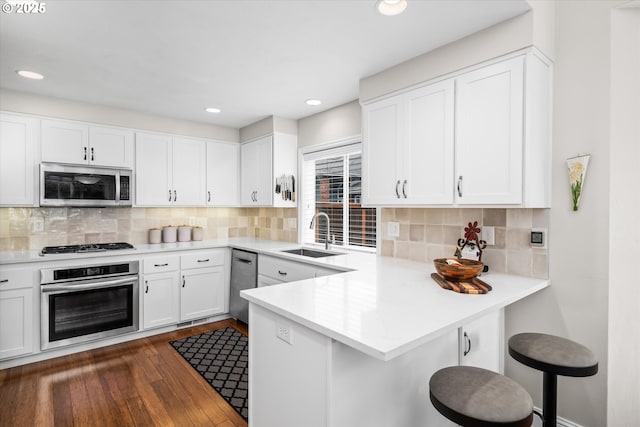 kitchen featuring appliances with stainless steel finishes, a sink, dark wood-style flooring, a peninsula, and white cabinetry