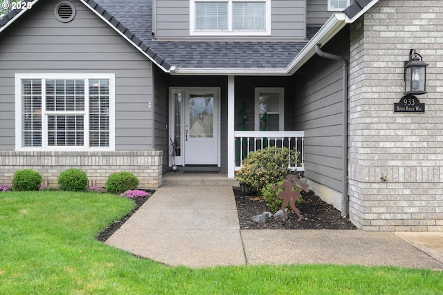 entrance to property featuring a shingled roof, covered porch, and a yard