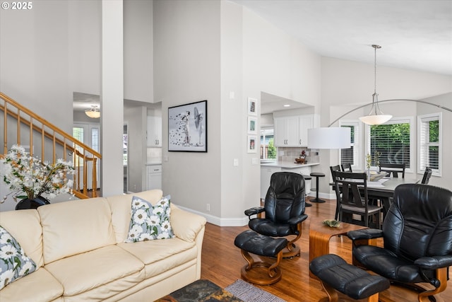 living area with healthy amount of natural light, wood finished floors, stairs, high vaulted ceiling, and baseboards