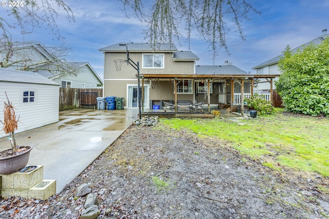 back of house featuring an outbuilding, covered porch, fence, and a lawn