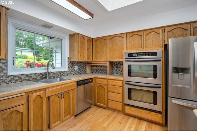 kitchen with stainless steel appliances, a sink, light wood-style flooring, tile counters, and backsplash