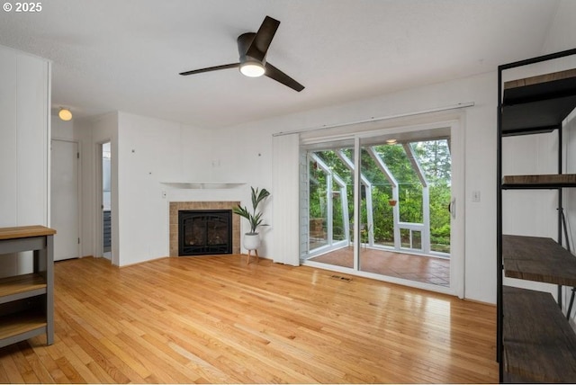 unfurnished living room with light wood-style flooring, ceiling fan, and a tiled fireplace