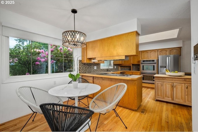 kitchen featuring appliances with stainless steel finishes, a peninsula, light wood-style floors, and brown cabinets