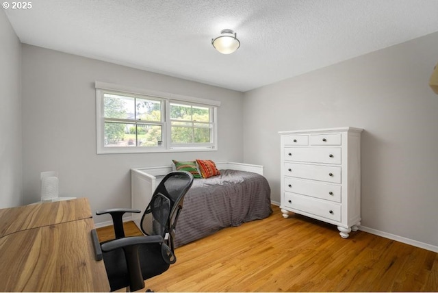 bedroom featuring light wood finished floors, baseboards, and a textured ceiling