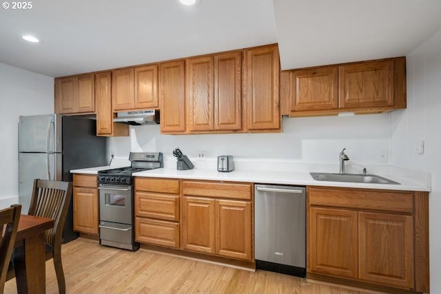 kitchen with stainless steel appliances, a sink, under cabinet range hood, light countertops, and light wood-type flooring