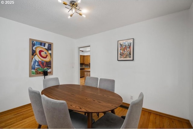 dining space with light wood-style floors, baseboards, and a textured ceiling
