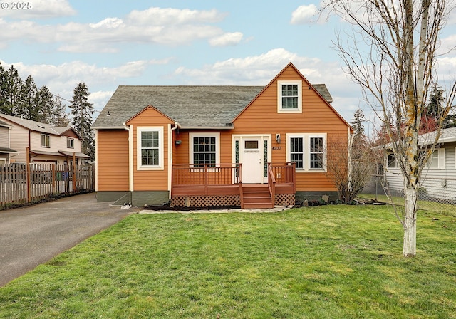 bungalow featuring a wooden deck, roof with shingles, a front yard, and fence