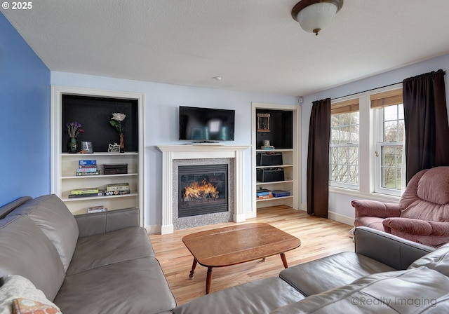 living area featuring built in shelves, baseboards, wood finished floors, a glass covered fireplace, and a textured ceiling