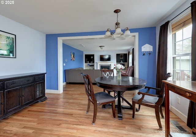 dining space with light wood-style flooring, a notable chandelier, baseboards, and a warm lit fireplace