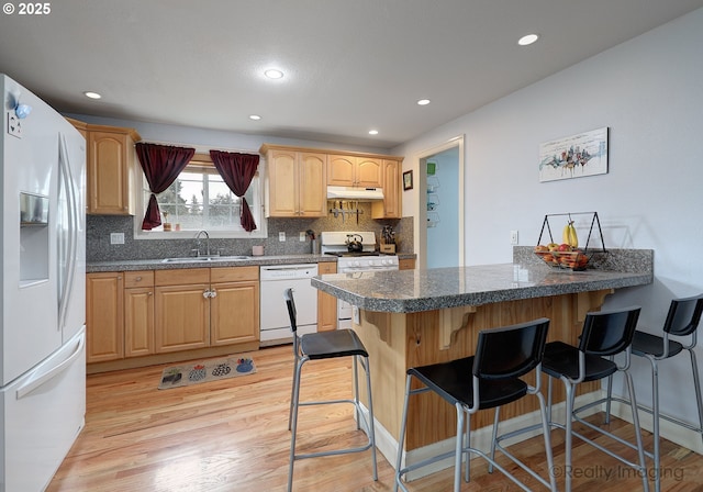 kitchen featuring a sink, under cabinet range hood, white appliances, a peninsula, and a breakfast bar area