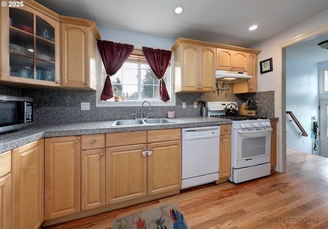 kitchen featuring white appliances, a sink, glass insert cabinets, under cabinet range hood, and backsplash