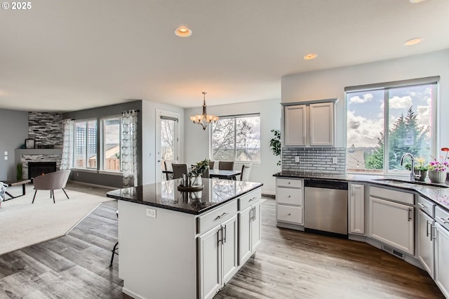 12998 SW Kostel Ln, Portland, OR 97224 - kitchen with stainless steel dishwasher, a sink, a stone fireplace, a chandelier, and open floor plan