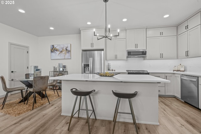 kitchen featuring appliances with stainless steel finishes, an inviting chandelier, light wood finished floors, and a center island