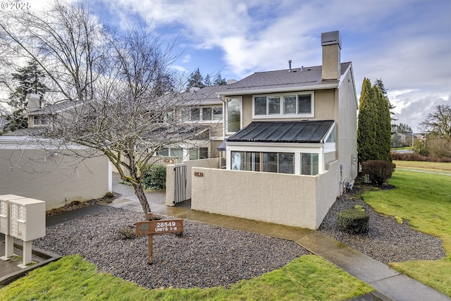 rear view of property with a chimney, metal roof, a standing seam roof, a yard, and stucco siding