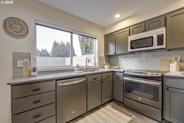 kitchen with stainless steel appliances, tasteful backsplash, light countertops, a sink, and light wood-type flooring