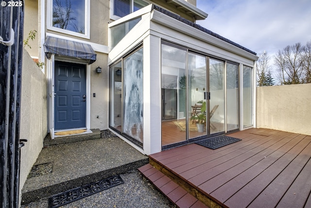 entrance to property with a wooden deck, fence, and stucco siding